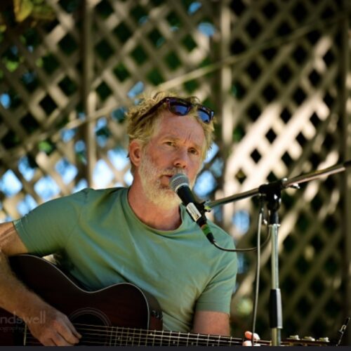 Drew McIvor sitting in behind a mic stand, singing and playing guitar